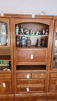 Full front view of the wooden bar cabinet showing the open arched shelf with various figurines not included, and multiple drawers below.