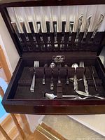 Open wooden cutlery canteen showing stainless steel forks, spoons, and knives arranged in slots with a black lining.