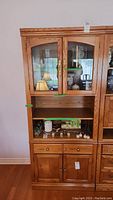 Front view of wooden display cabinet showing glass doors, open shelf, drawer, and lower wooden doors.