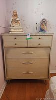 Front view of light wood four drawer dresser with religious statues on top