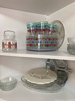 Colorful plastic patio glasses with matching large bowl, clear glass jar with floral design, ceramic plates with floral pattern, and oval glass tray.