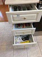 Photo showing three kitchen drawers with white fronts containing assorted kitchen utensils and cutlery.