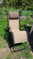 Front view of zero gravity lawn chair set outdoors on lawn with beige fabric, black frame, and brown cushioned headrest pillow.