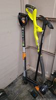 Photo of three garden tools standing cornered: Ryobi edger, Fiskars trimmer, Fiskars stand-up weeder