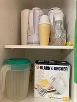 Shelf showing two insulated beverage jugs, a yellow plastic container, a green-lidded pitcher, and the boxed Black & Decker MX40 Mixmaster.