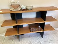 Full frontal view of three-shelf composite shelving unit showing light brown horizontal shelves and black vertical dividers.