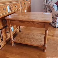 Side angle view of wooden side table showing turned legs and lower shelf.