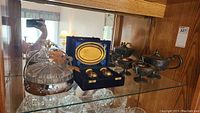 Display case with glass candy dish, miniature silver-plated tea set in blue case, and additional silver-plated pieces.