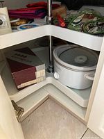 White Crock-Pot slow cooker inside kitchen cabinet, showing unit and next to boxes.