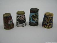 Four enamel sewing thimbles showing detailed colorful artwork and various designs including panda, butterfly, flowers.