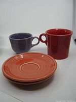 Four pieces of HLC Fiesta Ware USA including two cups and two plates against a plain white background.
