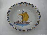 Full view of oval scalloped ceramic bowl showing painted blue and olive leaf border and central sailboat design.