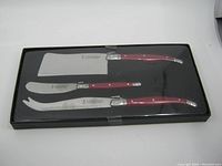 Full view of Laguiole cutting tool set in original black plastic box with clear lid showing all three cutting tools with red handles.