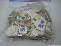Plastic bag filled with various old stamps attached to bits of paper and envelopes.