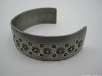 Front view of pewter bangle showing detailed punched circular floral designs.