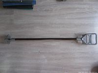 Full length view of the portable seat laid flat on the floor showing the wooden shaft with metal ends.