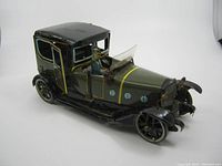 Left side perspective of the vintage metal wind up tin toy car showing the blue driver figure inside, open driver's side door, and detailed windshield.