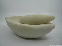 Side view of the marble mortar with pestle resting inside, showing overall shape and wear marks.