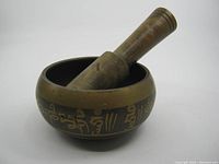 Angled view of Tibetan singing bowl with wooden mallet inside, showing engraved script on bowl exterior.