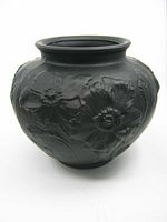 Front-side view of the black amethyst satin glass vase showing raised floral designs around the body, rounded shape with flared lip.