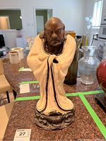 Front view of ceramic Bodhidharma figure on wooden stand