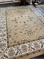 Full view of beige floral patterned area rug laid on hardwood floor showing detailed pattern and border design.