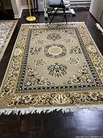 Full view of rectangular area rug laid on dark hardwood floor showing central medallion, floral motifs and white fringe.