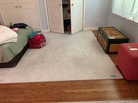 Full view of neutral colored area rug partially under bed and next to wood floor