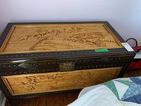 Front view of cedar chest closed showing relief carvings, metal latch and lacquered border.
