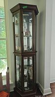 Front side view of tall wooden curio cabinet with glass display panels and door, shown empty of contents.
