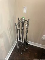 Full fireplace tool set with stand shown in corner of room on dark hardwood floor.
