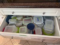 Drawer filled with many plastic and glass food storage containers of assorted shapes and sizes, some with lids and some without.