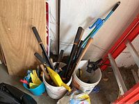Full view of various garden hand tools placed in two buckets including shovels, gloves, rake, and snips.