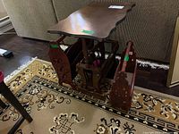 Three wood magazine racks including a rosewood one, one with a tabletop, and another carrying type rack on ornate carpet.