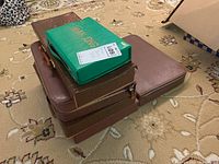 Stack of seven mahjong sets in cases on beige carpet, showing variety in case styles