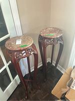 Two rosewood plant stands with round marble tops placed against a wall corner.