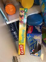 Photo shows Glad Cling Wrap 30 m in yellow packaging along with a torn box of Ziploc Snack bags in blue packaging and some round container lids in yellow, blue, orange.