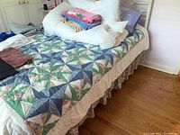 Full bed view showing quilt, white comforter and pillows with folded bedding on top