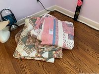 Two quilts folded and placed on wooden floor showing color and pattern details.