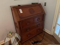 Closed slant-front desk showing carved circular motif on the drop-front panel and three lower drawers
