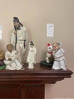Front view of five vintage Asian porcelain figurines on wooden surface, including tall man, children, and cat piggybank.