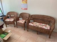 Photo showing full set of two armchairs and one loveseat with floral cushions on tiled floor against wall.