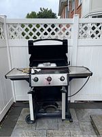 Grill with lid open showing side shelves, cooking grates and gas hose.