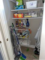 Full view of the laundry closet showing shelf with cleaning supplies, steam mop, dustpan, broom, towels and vacuum hose on the floor