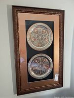 Full framed set of two artisan engraved Islamic plates behind glass with ornate bronze frame, set on black and tan mattes.