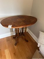 Full view of the oval side table showing the decorative inlaid top with floral patterns and the carved wooden legs.