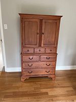 Front view of highboy dresser showing upper cabinet doors, three small drawers, two medium drawers, two larger drawers and bracket feet