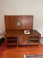 Full front view of the Ethan Allen TV entertainment unit with the detached back panel resting on top. Shows wood finish, two glass doors on sides, two center wooden drawers, and legs.