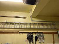 Full length of the 14-foot aluminum extension ladder stored horizontally on the garage wall, showing rungs and locking parts.
