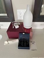 White Saje home incense diffuser standing on box with power cord, essential oils in front, and packaging box in background